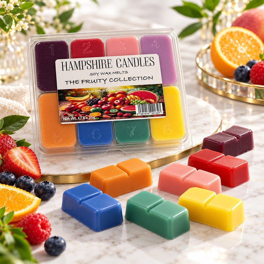 Bright Fruity Collection selection box on a marble board with loose melts, a halved orange, blueberries and strawberries