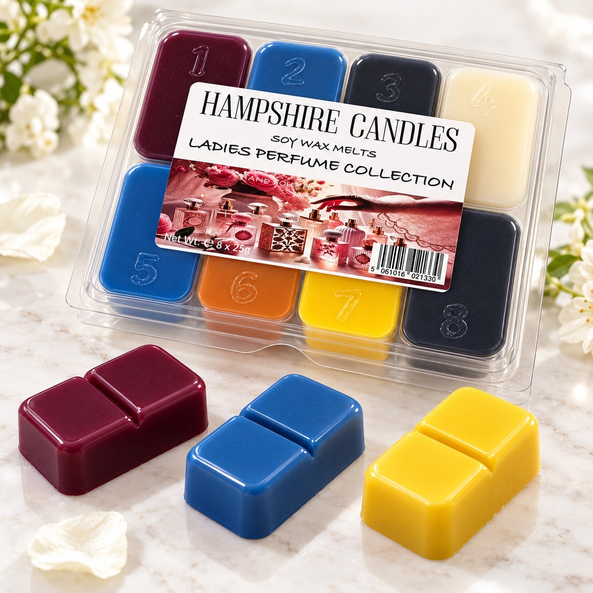 Close-up of the Perfume Collection gift box with loose burgundy, blue and yellow wax melts on white marble with petals