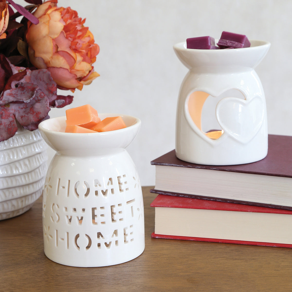 Two hearts and Home Sweet Home white ceramic wax burners with wax melts in the dishes, on a stack of books