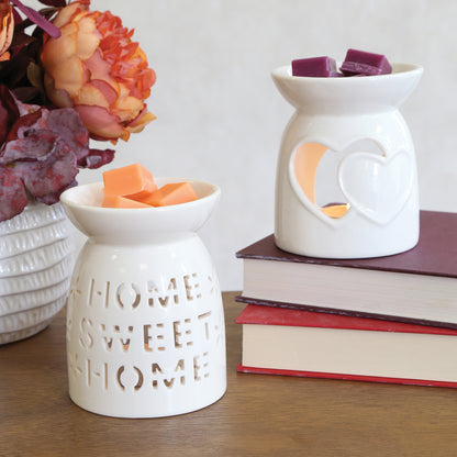 Two hearts and Home Sweet Home white ceramic wax burners with wax melts in the dishes, on a stack of books